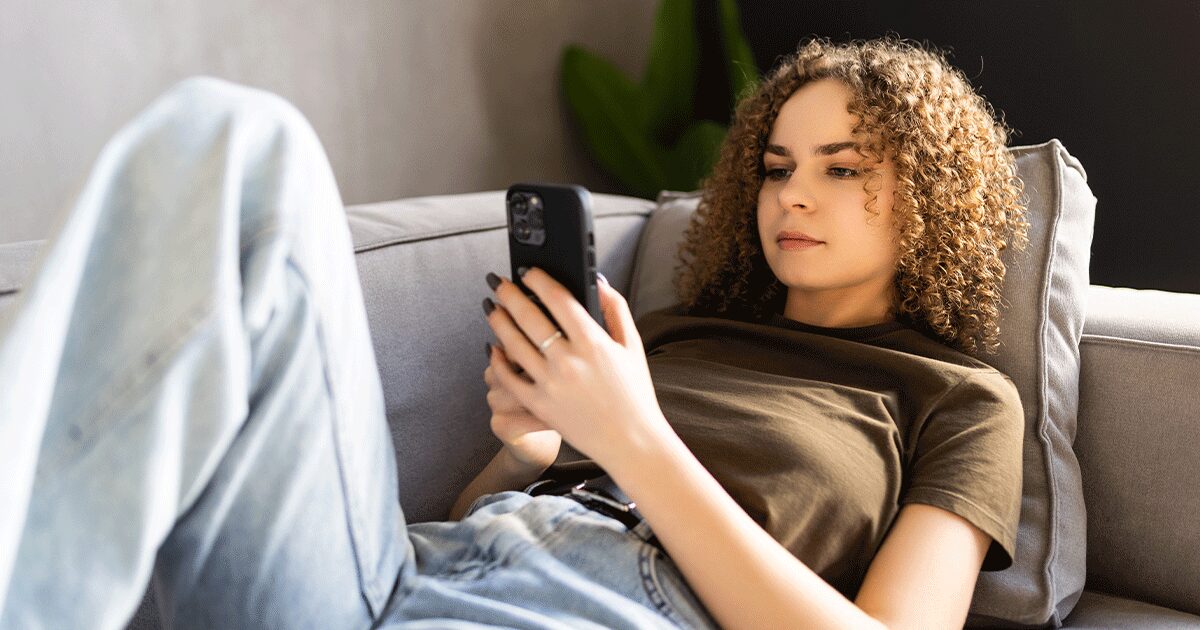 Young woman lying on a couch while researching on her phone before talking to her partner about an unplanned pregnancy.